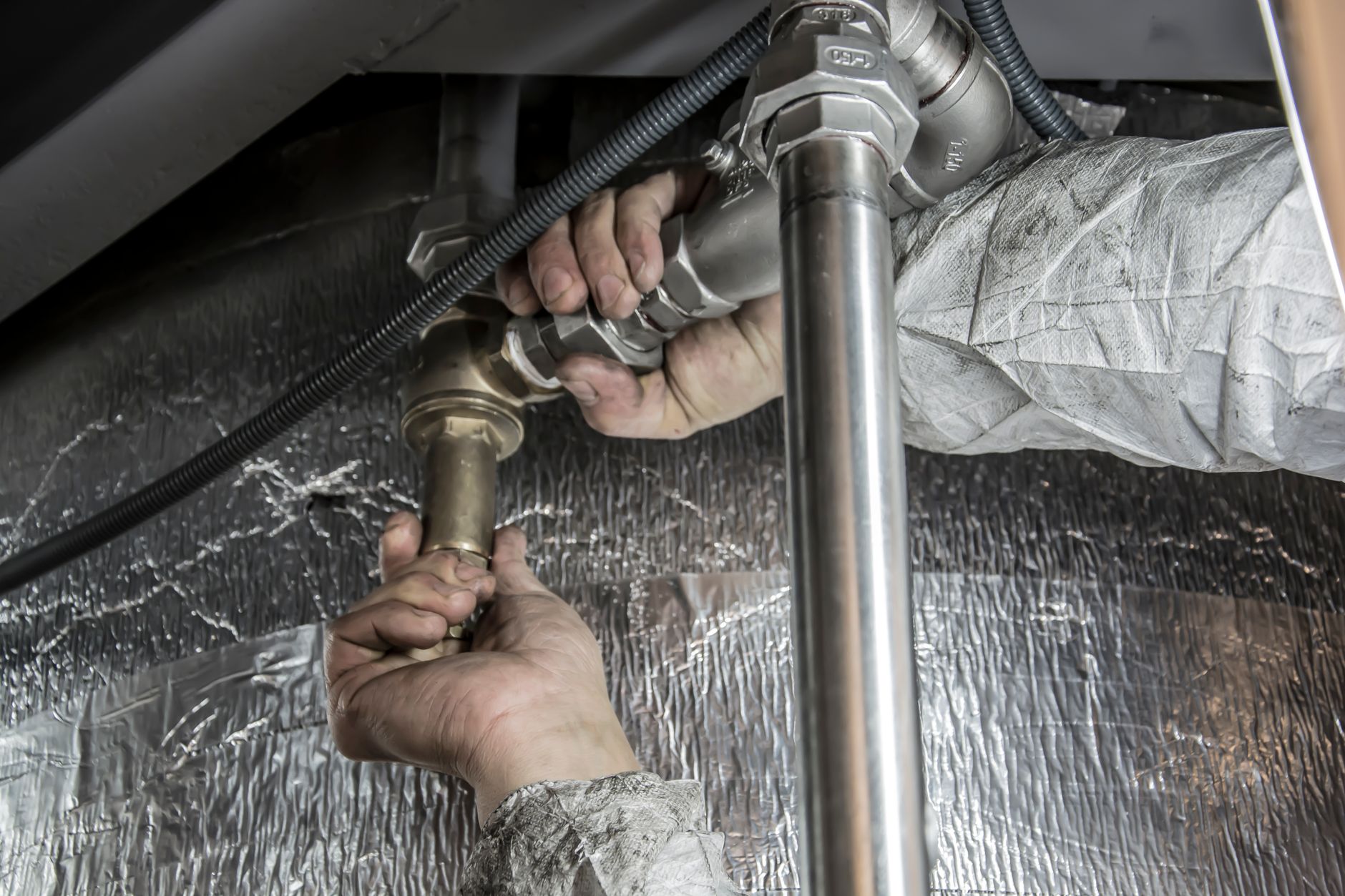 Hands fitting steel pipes and valves during an indoor installation